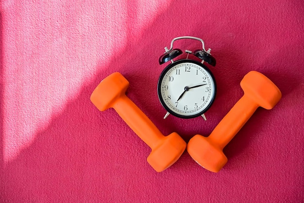 Фото Два оранжевых туннеля и будильник на розовом коврике для йоги время заняться фитнесом на самоизоляции занятия спортом дома с оборудованием