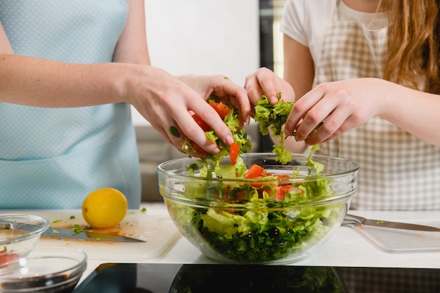 Two pair hands mix salad in bowl