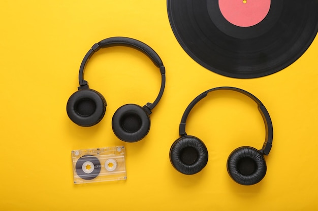 Two pairs of black stereo headphones vinyl records and audio
cassette on yellow background top view