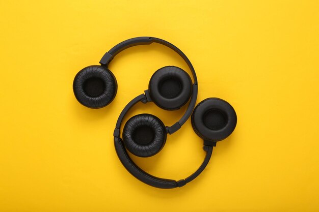 Two pairs of black wireless stereo headphones on yellow background Top view