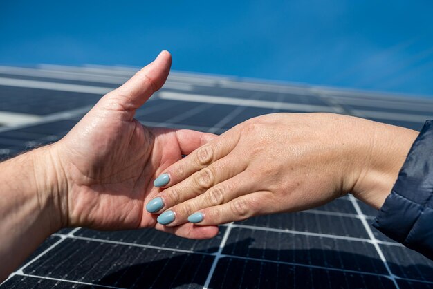 Two pairs of hands shaking hands after making a deal on the background of solar panels the concept of saving electricity