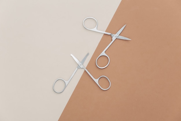 Two pairs of nail scissors on a beige-brown