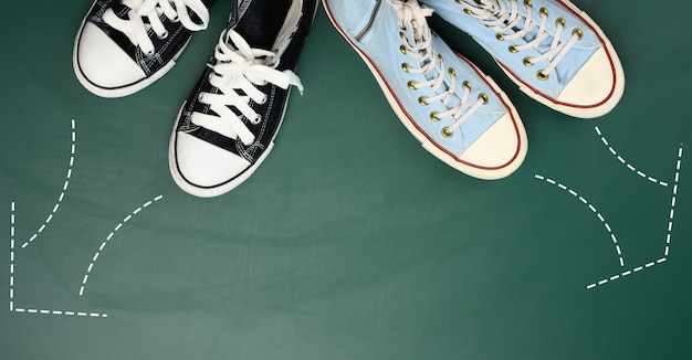 Two pairs of textile sneakers are directed in opposite directions. Quarrel and difference of opinion concept, different life paths and interests, top view