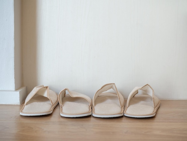 Two pairs of white soft slippers on wooden floor on white wall background