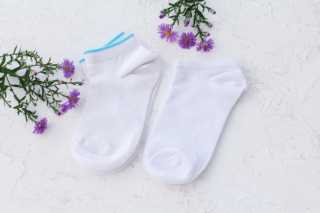 Two pairs of women socks and flowers on the white structured background, Top view.