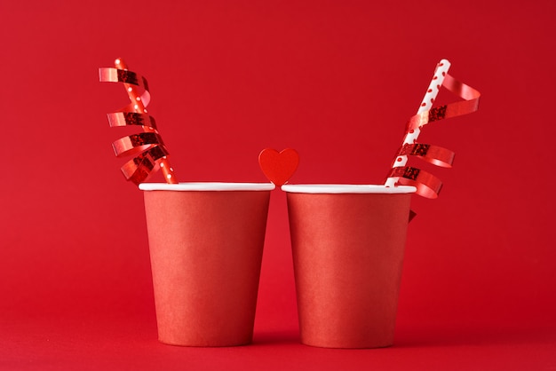 Two paper coffee cup with wooden heart and festive ribbons on red background.  Valentines day concept