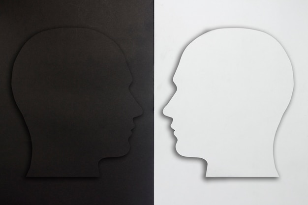 Two paper heads, black and white on a black and white background. The concept of a split personality, different opinions, dispute, war. Flat lay, top view.