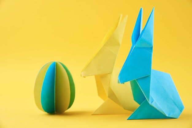 Two paper origami Esater rabbits and colored egg on a yellow wall. Easter celebration concept