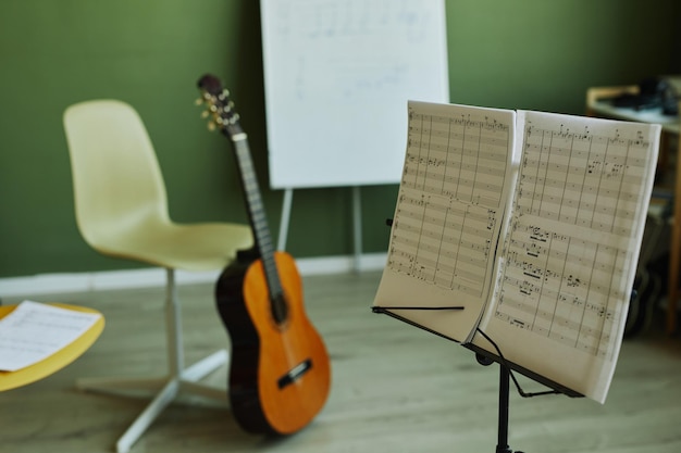 Two papers with musical notes on music stand on background of\
guitar chairs for students and whitebo