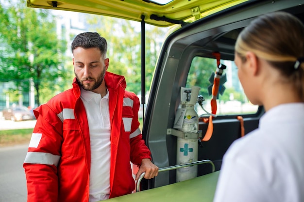 Foto due paramedici con una barella vicino ad un'ambulanza paramedici in uniforme che portano la barella fuori dall'ambulanza