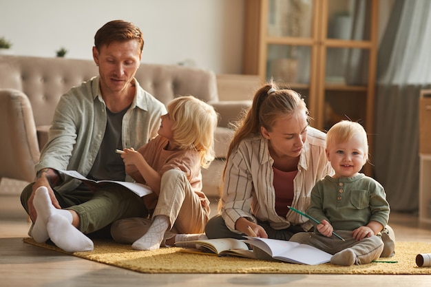 Due genitori seduti per terra e leggendo un libro ai loro figli piccoli nel soggiorno di casa