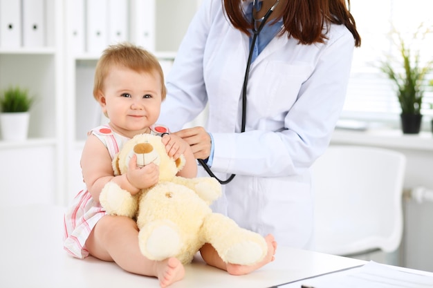 Two pediatricians are taking care of baby in hospital Little girl is being examining by doctor with stethoscope Health care insurance and help concept