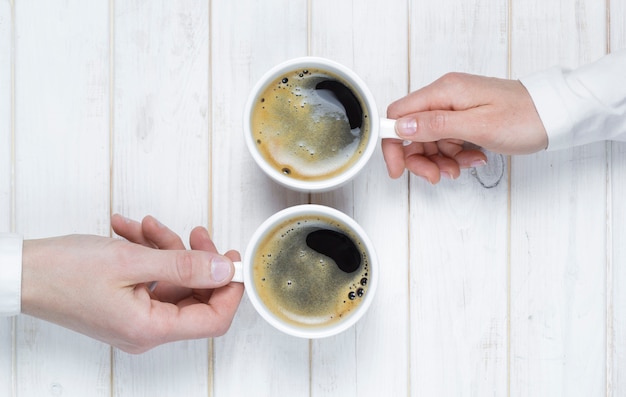 Two people are drinking coffee in cups. A hands holds cups 