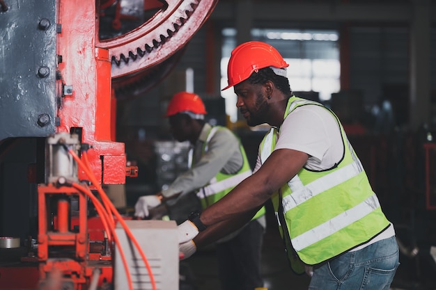 Two people black man African American worker control heavy machine in the factory
