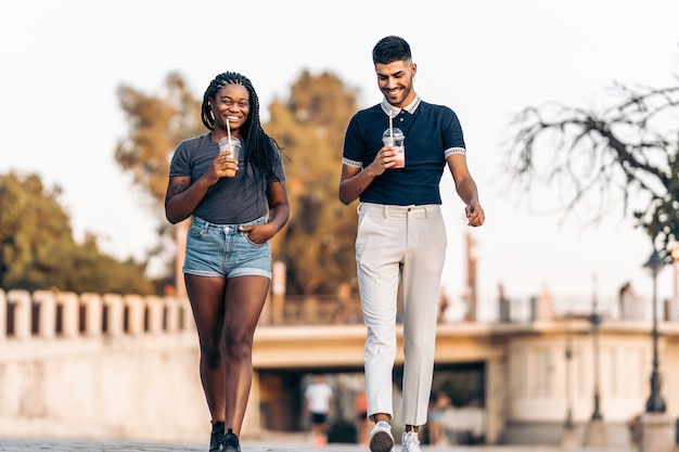 Two people of different ethnicities walking while drinking a shake in the street during summer