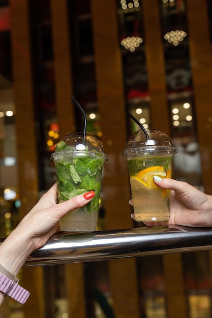 Два человека держат пластиковые стаканчики с напитками перед баром