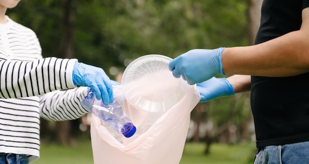 Two people keeping garbage plastic bottle into black bag at parkClearing pollution ecology and plastic concept xA