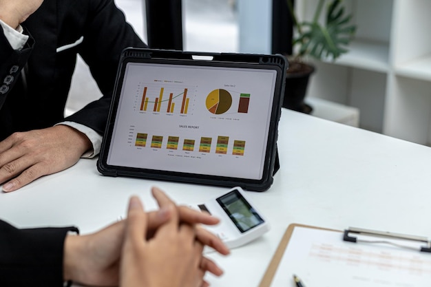 Two people look at the tablet screen showing the company financial summary, business people brainstorm ideas to solve losses and plan strategies to make the company profitable and grow.