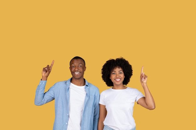 Two people pointing upwards smiling on yellow