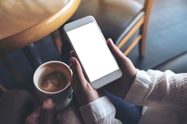 two people's hands holding mobile phone with blank desktop screen and a coffee