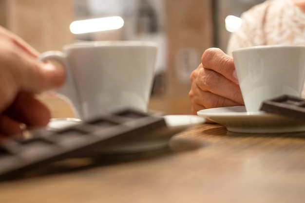 Two people's hands holding a white cup of coffee on a wooden table