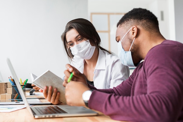 Photo two people working together in the office during pandemic with masks on