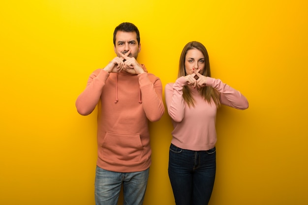 Photo two people on yellow background showing a sign of silence gesture