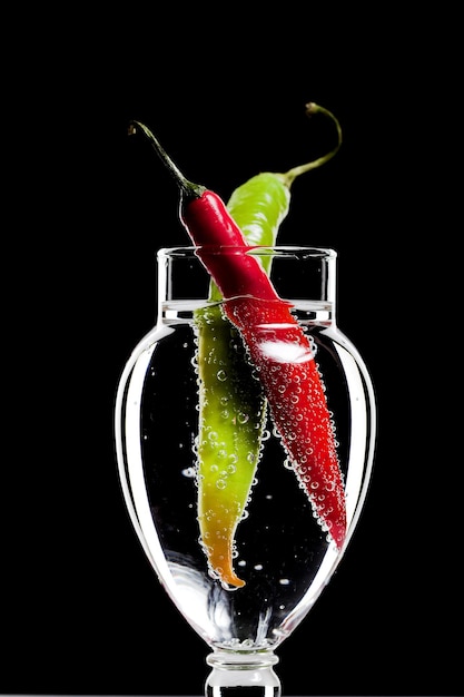 Two Peppers in The Glass of Bubbled Water Isolated on Black in Studio