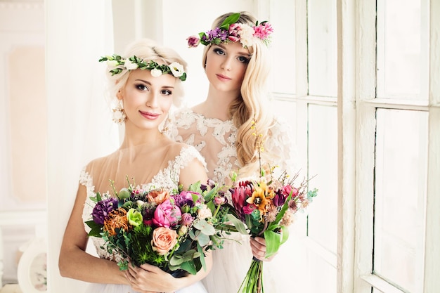 Two Perfect Bride Blonde Women with Flower Arrangement Flower Wreath Wedding Hairstyle and Makeup