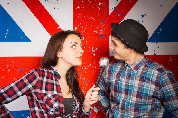 Two performers doing a British comedy show standing in front of a Union Jack painted on a wall using a microphone wearing patriotic clothing and a bowler hat