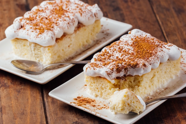 Foto due pezzi di un delizioso dessert di tre torte di latte su uno sfondo di legno