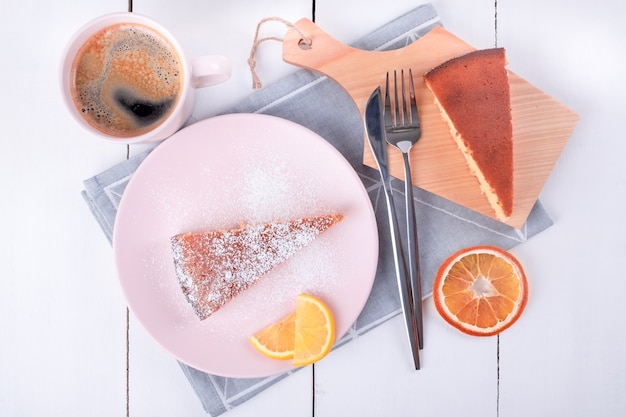 Due pezzi di torta su un piatto rosa e un tagliere con coltello e forchetta su un tovagliolo di lino piegato e una tazza con caffè