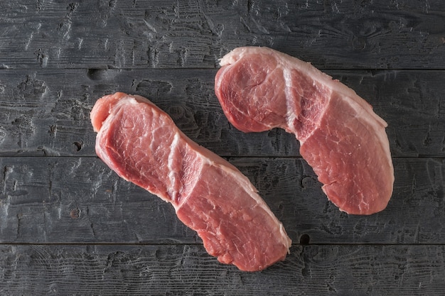 Due pezzi di carne di maiale su un tavolo di legno nero. ingredienti per la cottura di piatti di carne.