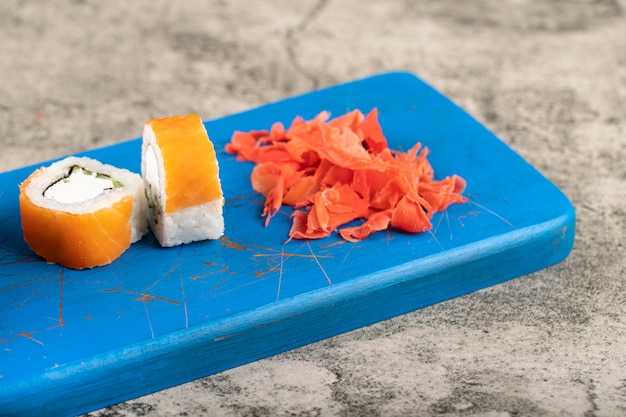 Two pieces of salmon sushi rolls and ginger on blue board