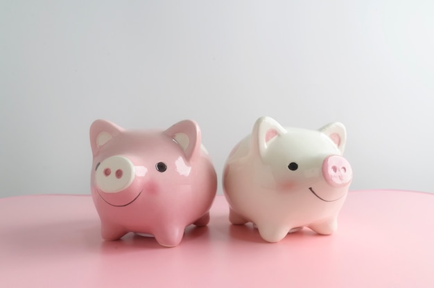 Two piggy bank on pink table with white background. A saving money for future investment concept.