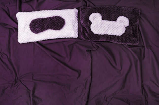 紫の綿のシーツが付いたベッドで毛皮から寝るための2つの枕と2つのアイマスク