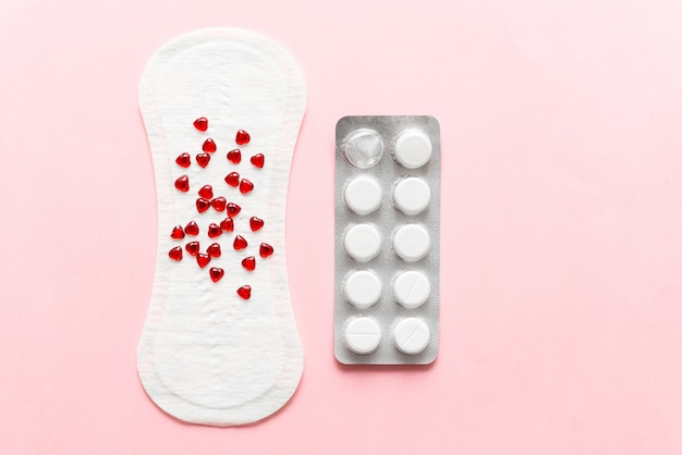 Two pills and menstruation pad with red hearst on it, painkiller contraception concept