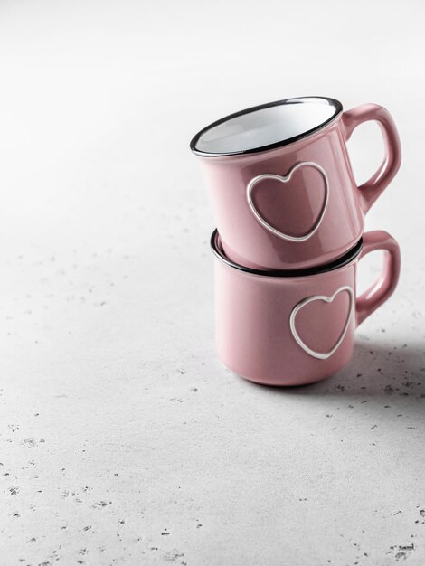 Two pink cups with hearts on white textured background for St Valentines day Vertical orientation
