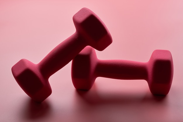 Two pink female dumbbells isolated on pink background close-up with copy space. Fitness concept, weight loss and sport activity