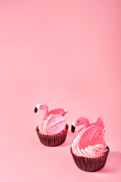 パステル ピンクの背景にお誕生日おめでとうカード クローズ アップ コピー スペースに 2 つのピンクのフラミンゴのカップケーキ