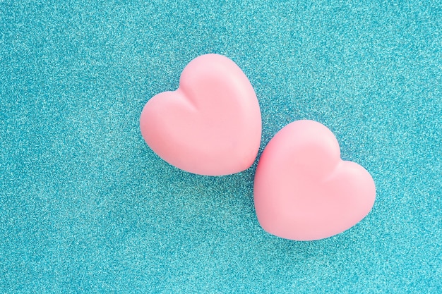 Two pink glittering hearts on a blue glittering background