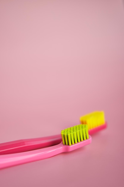 Two pink toothbrushes stand in pink glass on pink background together One brush is new and other old