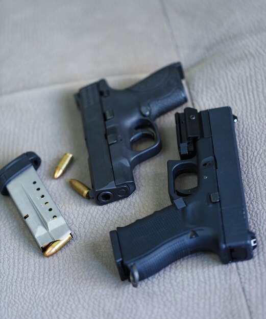 사진 회색 바탕에 9mm 총알이 장착된 두 개의 권총 검은색 소총과 앞에 9mm 총알이 장착된 카메라가 총알과 총알의 입구에 초점을 맞추고 있습니다.