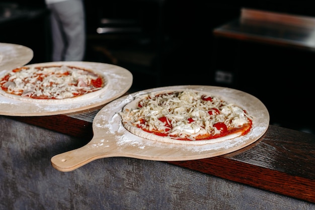 Two pizzas on a counter with one being uncooked.