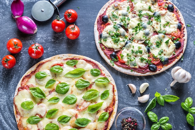 Two pizzas with ingredients on the wooden surface