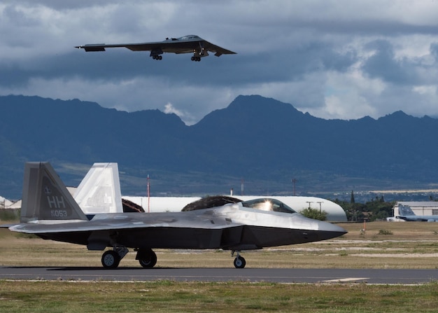 Two planes are on a runway with one being flown by a fighter jet.