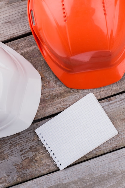 two plastic constructor workers helmets and notepad for copy space. top view close up.
