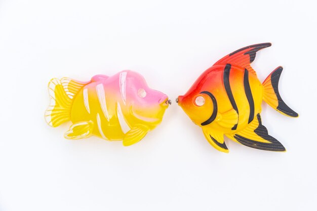 Two plastic fish lie on a white background facing each other.