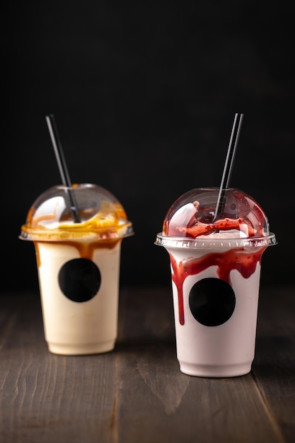 Two plastic glasses of tasty milkshake on dark wooden backgroundCopy space