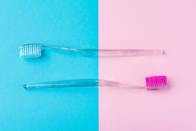 Two plastic toothbrushes on a pastel blue and pink  background, flat lay style